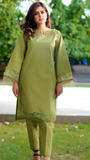 Woman wearing a green traditional outfit with floral embroidery in an outdoor setting.